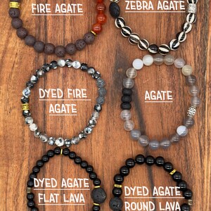 May include: Six different bracelets made with various types of agate and lava beads. The bracelets feature gold accents and are arranged in two rows of three. The bracelets are labeled with their names: Fire Agate, Zebra Agate, Dyed Fire Agate, Agate, Dyed Agate Flat Lava, and Dyed Agate Round Lava.