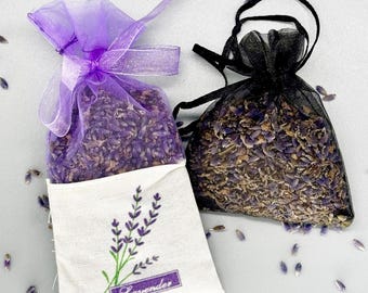May include: Two lavender sachets, one in a white fabric bag with a lavender design and the word "Lavender" printed on it, and the other in a black mesh bag. Both bags are filled with dried lavender flowers.