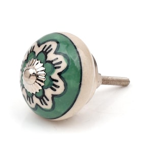 Könnte beinhalten: Ein runder Möbelknopf aus Keramik mit einem grün-weißen Blumenmuster, einer mittigen silberfarbenen Metallkappe und einem Gewindebolzen aus Metall, der an der Rückseite zur Montage an Möbeln oder Schubladen herausragt.