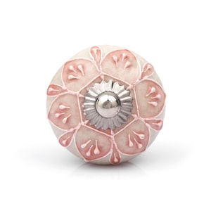 May include: A cream-coloured cabinet knob with a pink floral pattern. The round knob has a silver-coloured, star-shaped metal centre. The floral design is raised, creating a textured surface.