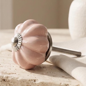 May include: A pale pink ceramic cabinet knob with a rounded, fluted pumpkin shape and a silver-toned metal centre cap. The knob features a long, threaded metal bolt extending from the back, designed for attachment to furniture or cabinetry doors.