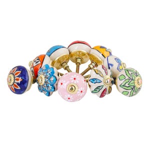 May include: A collection of decorative ceramic cabinet knobs. The knobs feature various colorful designs, including floral patterns, stripes, and abstract shapes. Each knob has a brass base and screw. The color palette includes blue, pink, yellow, and green.