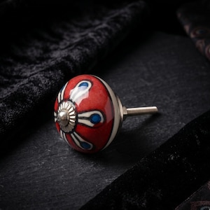 Könnte beinhalten: Dekorativer Schrankknopf mit einem roten, weißen und blauen Blumendesign. Der Keramikknauf hat eine silberne Metallbasis und eine Schraube. Der Knauf hat eine runde Form und eignet sich für Möbel oder die Inneneinrichtung.