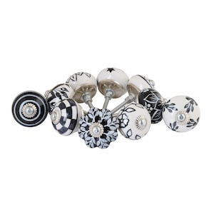 May include: A collection of decorative ceramic cabinet knobs in various designs. The knobs feature black and white patterns, including stripes, floral, and geometric shapes. Each knob has a silver-toned metal base.