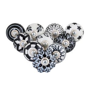 May include: A collection of decorative ceramic cabinet knobs in various black and white patterns. Designs include floral, star, and geometric motifs. Each knob has a silver-toned metal base.