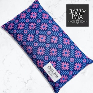 May include: A rectangular, navy blue heat pack with a floral pattern in pink and blue. The pattern features stylized flowers and leaves. A white label with the text "JAZZY PAX" is attached to the pack.