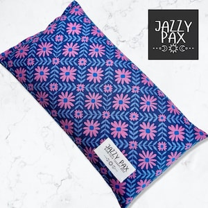 May include: A rectangular, navy blue aromatherapy pillow with a floral pattern in pink and light blue. The pillow features a repeating design of stylized flowers and leaves. A white label with the text "JAZZY PAX" is attached to the pillow.