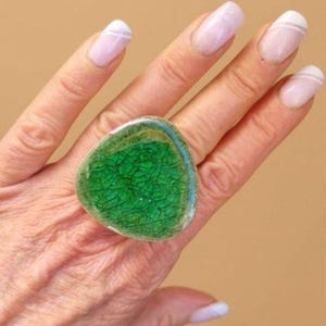 Peut inclure: Une bague dotée d'une grande pièce centrale de forme triangulaire irrégulière avec une finition émaillée vert vif craquelé. La surface de l'élément présente un réseau distinct de fines lignes sombres sur la couleur verte éclatante.