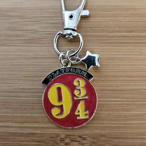 May include: A silver-colored keychain with a lobster clasp and a charm featuring the words "PLATFORM" above the numbers "9 3/4" in yellow on a red background. A small star charm hangs below the clasp.
