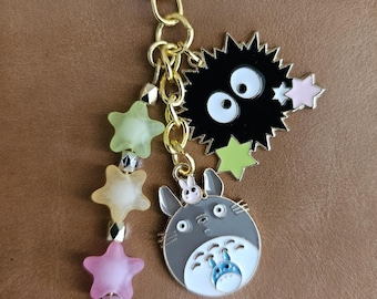 May include: A gold-colored keychain with multiple charms. Charms include a star, a black soot sprite, and a gray Totoro character. Additional charms are star-shaped and in shades of pink, yellow, and green.