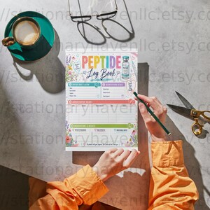 Può includere: Un registro Peptide Log Book con bordi floreali e un'illustrazione di una fiala, con sezioni per dettagli di iniezione, concentrazione e note. La pagina include il testo Peptide Log Book e viene compilata con una penna verde scuro.