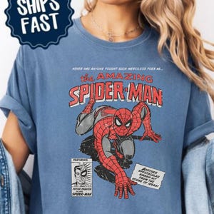 K&ouml;nnte beinhalten: Blaues Jeans-T-Shirt mit einem Vintage-Comic-Grafik von Spider-Man. Das Design enth&auml;lt den Text "the AMAZING SPIDER-MAN" und weitere Comic-Elemente. Das Shirt hat auch den Text "COMFORT COLORS - BLUE JEAN".