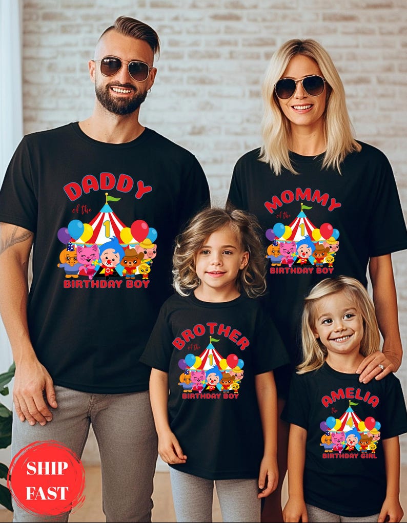 K&ouml;nnte beinhalten: Schwarze T-Shirts f&uuml;r eine Familie, jedes mit einem Geburtstagsthema. Die Shirts zeigen ein Zirkuszelt-Design mit Cartoon-Figuren und den Texten "Daddy", "Mommy", "Brother" und "Amelia the Birthday Girl". Ballons und farbenfrohe Akzente vervollst&auml;ndigen das Design.