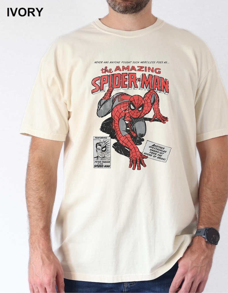 K&ouml;nnte beinhalten: Elfenbeinfarbenes T-Shirt mit einem Comic-Motiv von Spider-Man. Das Design enth&auml;lt den Text "the AMAZING SPIDER-MAN" in Rot und Wei&szlig; sowie weitere Texte und Illustrationen. Das T-Shirt hat kurze &Auml;rmel.