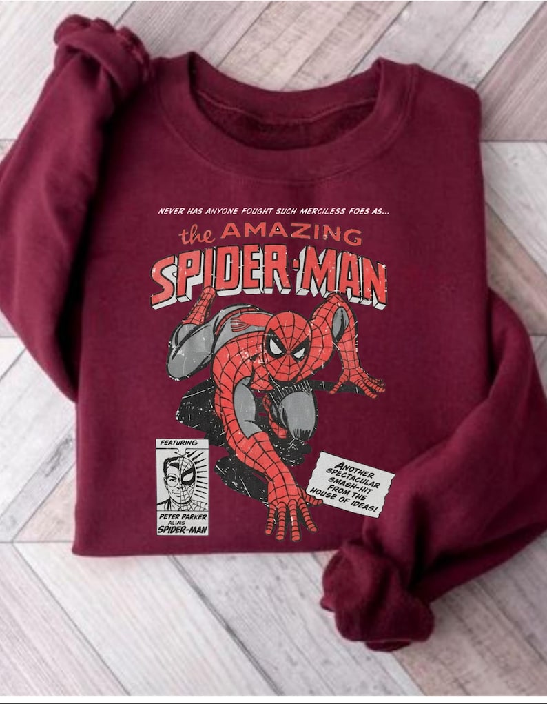 K&ouml;nnte beinhalten: Burgunderfarbenes Sweatshirt mit einem Vintage-Comic-Stil-Grafik von Spider-Man. Das Design enth&auml;lt den Text "the AMAZING SPIDER-MAN" und Textfelder mit "PETER PARKER" und "HOUSE OF IDEAS!"