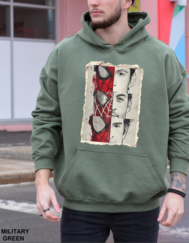 Op de afbeelding: Militairgroene hoodie met een grafische print van Spider-Man. De print staat op een verweerde achtergrond. De hoodie heeft een kangoeroezak en een capuchon met trekkoord. De tekst "MILITARY GREEN" staat onderaan.