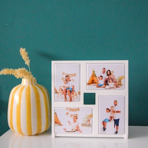 May include: A white multi-photo frame with four picture slots and a small square opening. The frame holds family photos. A yellow and white striped vase with dried flowers sits to the left. The background is a teal wall.