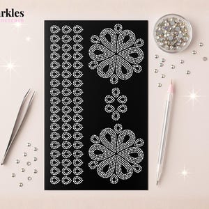 Pode incluir: Uma folha preta com desenhos de strass brancos, incluindo padrões florais e de lágrimas, juntamente com uma pequena tigela de strass, pinças e uma caneta. A imagem é intitulada "Sparkles by Junetrain".