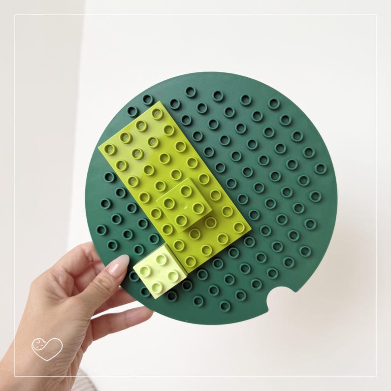 Dunkelgrüne Bauplatte wird von einer Hand gehalten, bestückt mit transparent-gelben DUPLO®-Steinen.