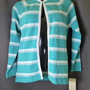 May include: A long-sleeved open-front cardigan featuring horizontal stripes in turquoise and white. The garment has a round neckline with white trim along the front edges and cuffs. A beige paper tag is attached to the bottom right hem.