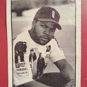 May include: Black and white poster featuring a man wearing a baseball cap with a zig-zag design and a white t-shirt with the text "STREET KNOWLEDGE PRODUCTIONS INC." and images of people. The poster also has the text "ST. IDES PREMIUM MALT LIQUOR".