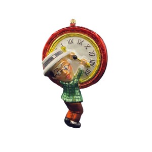 May include: A glass Christmas ornament featuring a cartoon man in a green plaid shirt and a white hat holding a red clock with Roman numerals.