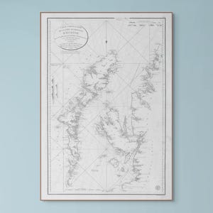 Puede incluir: Impresión enmarcada de un mapa antiguo en escala de grises, que representa una región costera detallada con líneas y texto intrincados. El mapa está encerrado en un marco de madera simple, creando una estética clásica.