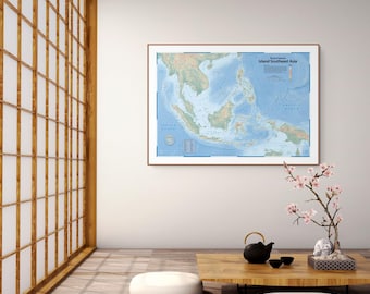 May include: A framed physical map titled Island Southeast Asia featuring detailed topography of the region in shades of green and blue, displayed on a white wall above a low wooden table with a black teapot and a small flowering branch.
