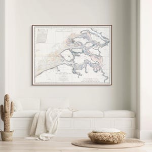 Könnte beinhalten: Eine gerahmte Vintage-Karte eines Küstengebiets mit detaillierten Illustrationen von Wasserwegen und Landmassen. Die Karte befindet sich in einem braunen Rahmen und hat einen cremefarbenen Hintergrund mit blauen und rosa Akzenten. Die Karte wird über einer weißen Bank angezeigt.