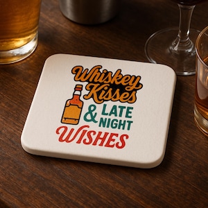 May include: Square, off-white coaster with the text "Whiskey Kisses & Late Night Wishes" in orange, green, and red. A cartoon whiskey bottle is also featured. The coaster is on a dark wood surface.