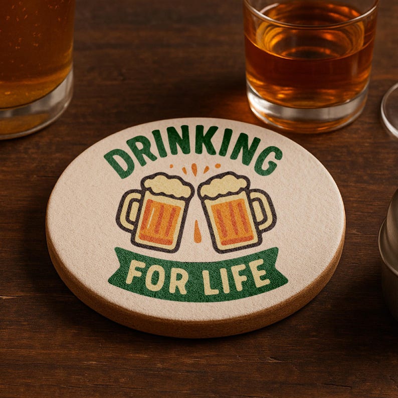 May include: Round coaster with the text "DRINKING FOR LIFE" in green and white. The coaster features two cartoon beer mugs with orange beer and white foam. The coaster is beige with a brown edge.