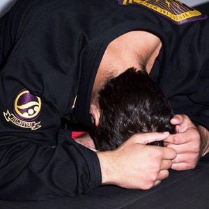 Puede incluir: Una persona vistiendo un uniforme negro de artes marciales con bordados dorados y morados. El uniforme tiene las palabras "From The Inside Out" y "Jiu Jitsu" en él.