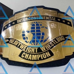 Puede incluir: Un cinturón de campeonato de lucha libre dorado y negro con las palabras "Intercontinental Heavyweight Wrestling Champion" y un diseño de globo terráqueo azul.