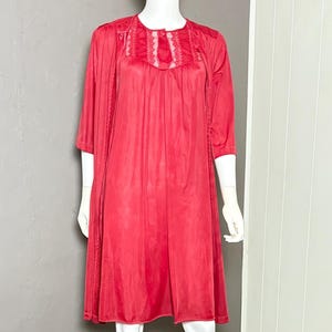 May include: A red vintage nightdress and robe set on a mannequin. The nightdress is knee-length with a lace-trimmed neckline. The robe has three-quarter sleeves and matching lace detail. The set is made of a shiny, lightweight fabric.