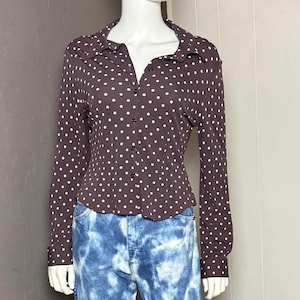 以下が含まれることがあります： マネキンが、白い水玉模様の茶色のボタンダウンシャツと、青いタイダイジーンズを着用しています。 シャツは長袖と襟付きです。 ジーンズは、ユニークな白い模様のライトブルーウォッシュです。 サイズはセンチメートルです。