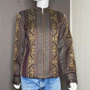 May include: A long-sleeved jacket featuring a mandarin collar and a full-length front zipper. The garment displays a complex, multi-colored pattern in shades of gold, brown, and dark purple, with vertical panels of intricate geometric and floral motifs.