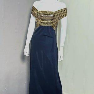 Può includere: Abito da sera nero su un manichino. Il corpetto è impreziosito da paillettes e perline dorate, e lo scollo a spalle scoperte aggiunge un tocco di eleganza. L'abito ha una gonna lunga.