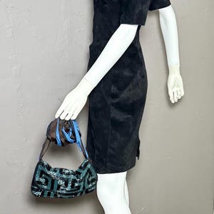 May include: A black dress with short sleeves and a small, patterned handbag with blue and green sequins. The handbag has a blue strap and is held by a mannequin.