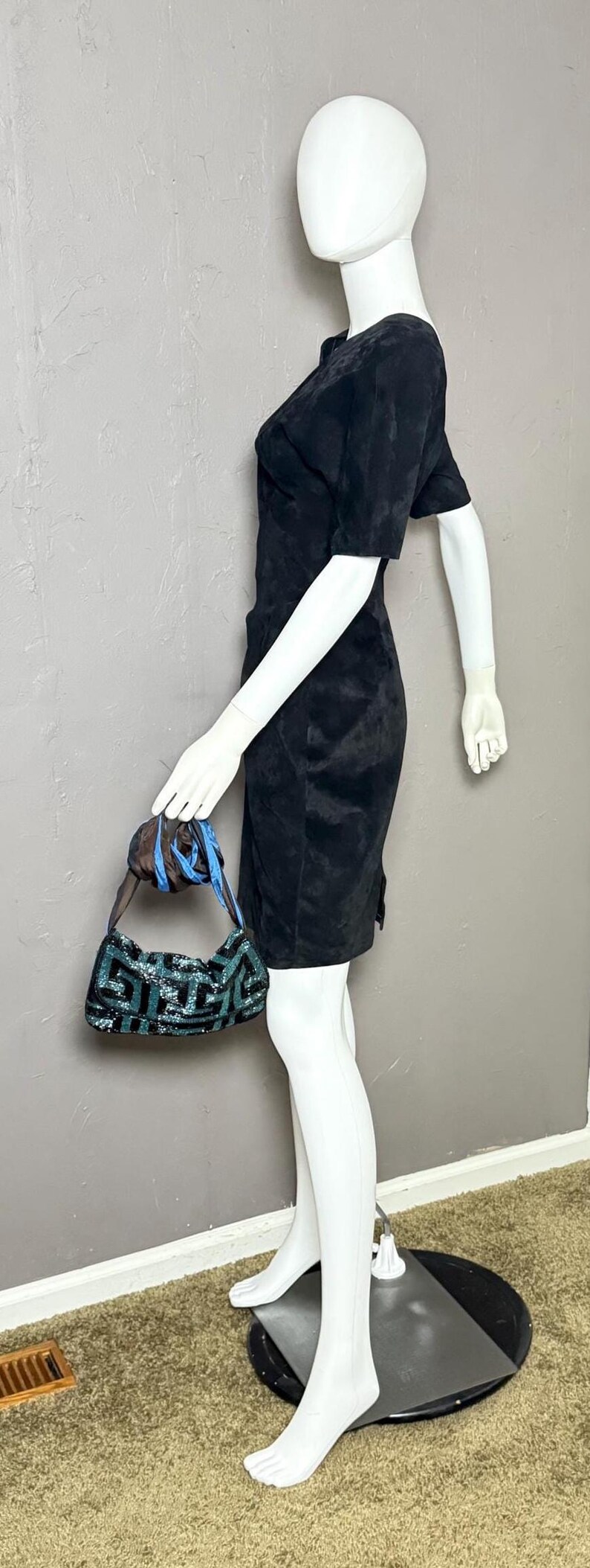 May include: A black dress with short sleeves and a small, patterned handbag with blue and green sequins. The handbag has a blue strap and is held by a mannequin.