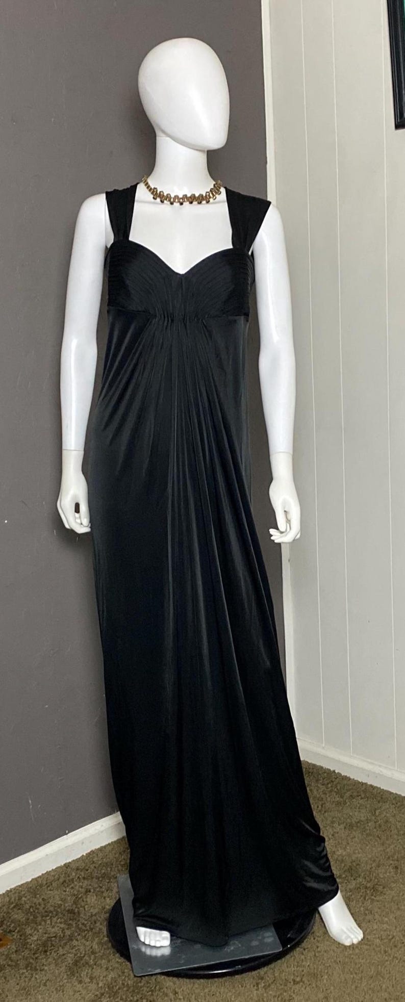 K&ouml;nnte beinhalten: Ein bodenlanges schwarzes Kleid an einer Schaufensterpuppe. Das Kleid hat einen herzf&ouml;rmigen Ausschnitt und ein eng anliegendes Oberteil, das in einen weiten Rock &uuml;bergeht. Eine goldfarbene Halskette schm&uuml;ckt den Hals der Schaufensterpuppe. Das Kleid ist aus weichem, flie&szlig;endem Stoff gefertigt.