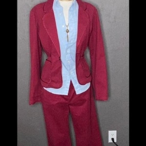 May include: A burgundy blazer and matching pants suit. The blazer has a notched collar and a single button closure. The pants have a straight leg.