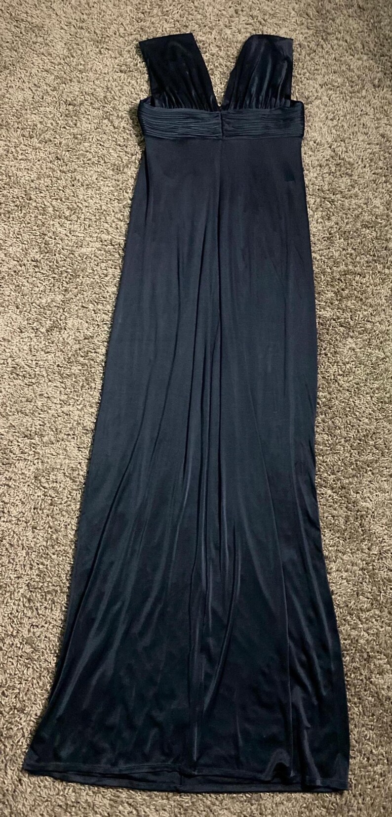 K&ouml;nnte beinhalten: Ein langes, dunkelmarineblaues Kleid mit V-Ausschnitt. Das Oberteil hat ein gerafftes Detail, und das Kleid flie&szlig;t bis zum Boden. Der Stoff scheint ein weiches, samtartiges Material zu sein.