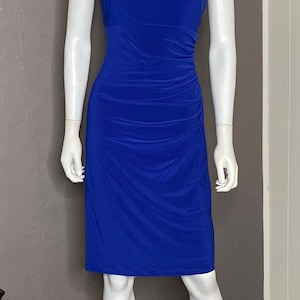 May include: A royal blue dress on a mannequin. The dress has a ruched bodice and a knee-length hemline. The shoulders are decorated with sparkling embellishments. The dress is displayed on a white mannequin against a grey wall.