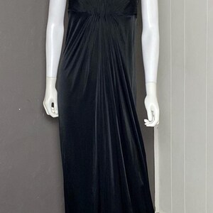 K&ouml;nnte beinhalten: Ein schwarzes Abendkleid auf einer Schaufensterpuppe. Das Kleid hat einen herzf&ouml;rmigen Ausschnitt, ein eng anliegendes Oberteil und einen flie&szlig;enden Rock. Eine goldfarbene Halskette schm&uuml;ckt den Hals der Schaufensterpuppe. Das bodenlange Kleid ist aus weichem, drapierendem Stoff gefertigt.