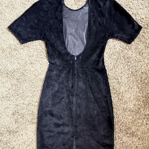 May include: A dark navy blue dress with short sleeves and a low back. The dress has a zipper down the back and a slit at the bottom. The fabric appears to be suede or a similar material.