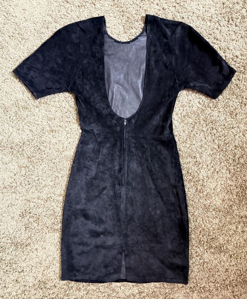 May include: A dark navy blue dress with short sleeves and a low back. The dress has a zipper down the back and a slit at the bottom. The fabric appears to be suede or a similar material.