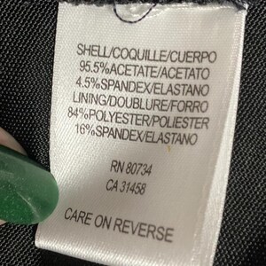 K&ouml;nnte beinhalten: Ein wei&szlig;es Kleidungsetikett mit schwarzem Text, das die Stoffzusammensetzung angibt: Prozents&auml;tze von Acetat, Elasthan und Polyester. Das Etikett enth&auml;lt auch den Text "CARE ON REVERSE" und die Nummern RN 80734 und CA 31458.
