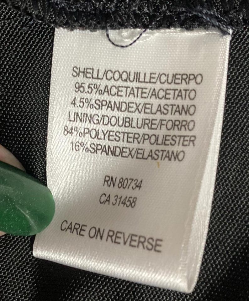 K&ouml;nnte beinhalten: Ein wei&szlig;es Kleidungsetikett mit schwarzem Text, das die Stoffzusammensetzung angibt: Prozents&auml;tze von Acetat, Elasthan und Polyester. Das Etikett enth&auml;lt auch den Text "CARE ON REVERSE" und die Nummern RN 80734 und CA 31458.