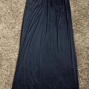 K&ouml;nnte beinhalten: Ein dunkelmarineblaues Abendkleid mit V-Ausschnitt und flie&szlig;endem, bodenlangem Design. Das Oberteil hat plissierte Details, und der Stoff f&auml;llt elegant. Das Kleid ist aus einem weichen, flie&szlig;enden Material gefertigt, das sich f&uuml;r besondere Anl&auml;sse eignet.