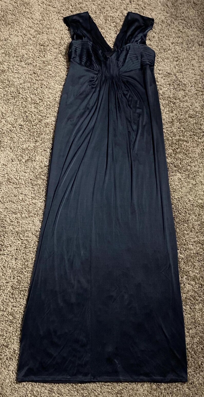 K&ouml;nnte beinhalten: Ein dunkelmarineblaues Abendkleid mit V-Ausschnitt und flie&szlig;endem, bodenlangem Design. Das Oberteil hat plissierte Details, und der Stoff f&auml;llt elegant. Das Kleid ist aus einem weichen, flie&szlig;enden Material gefertigt, das sich f&uuml;r besondere Anl&auml;sse eignet.